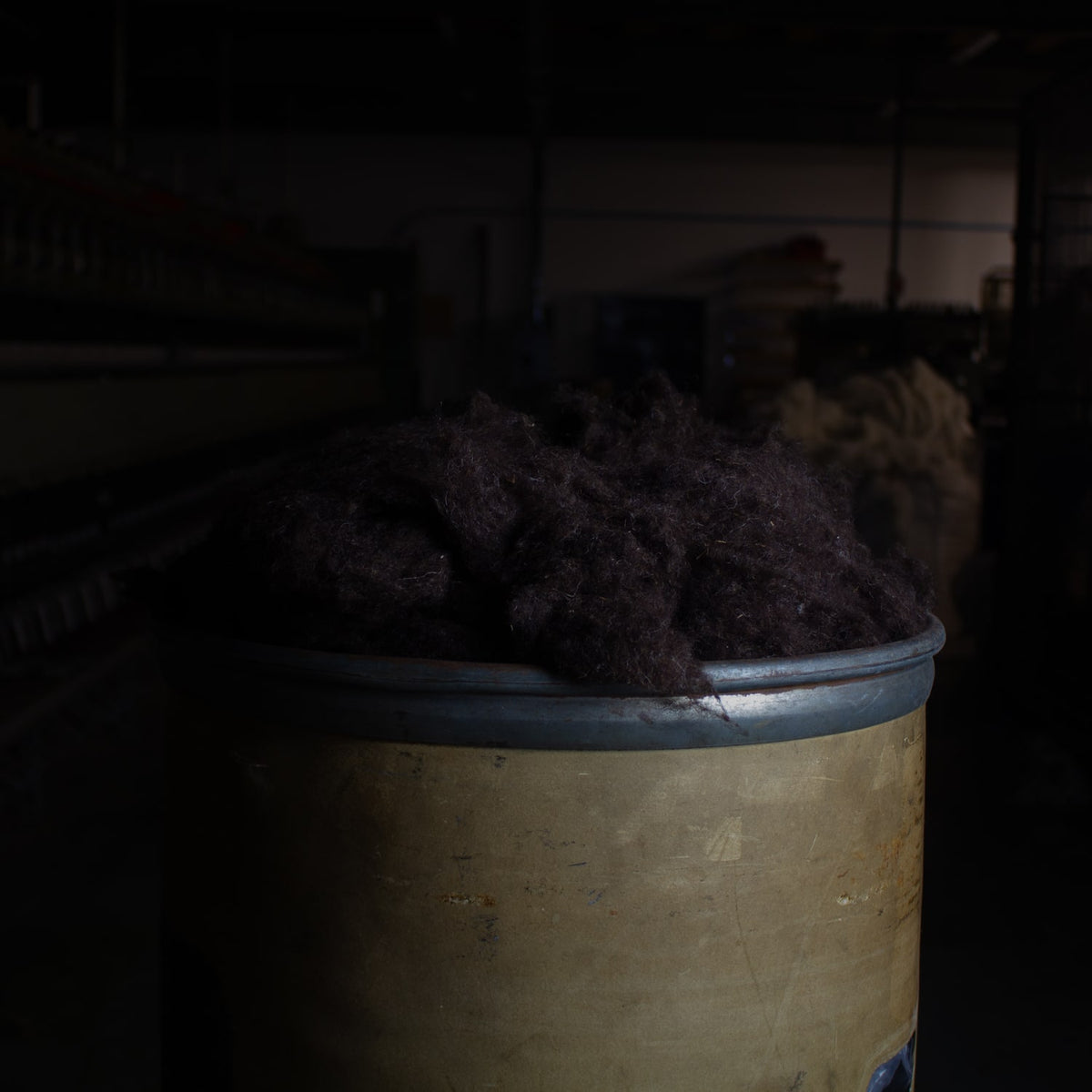 A sliver can is pictured overflowing with wool noil in natural black, used as organic wool stuffing